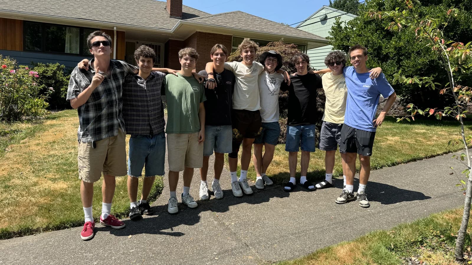 Nine longtime friends standing together outside on a sunny day.